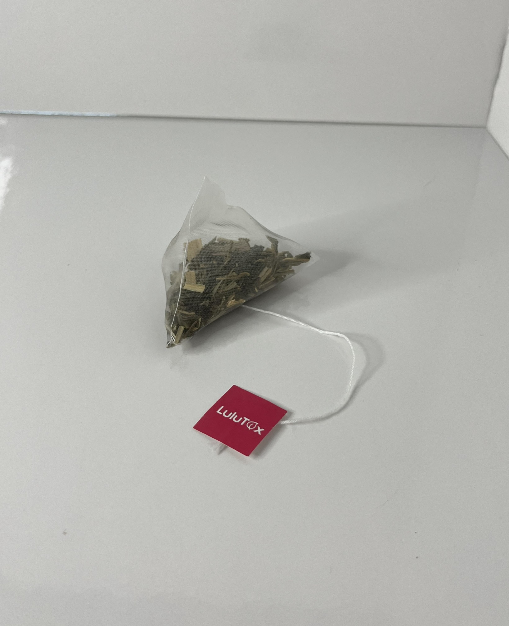 The tea bag is positioned from the side, emphasizing its triangular form and tag placement.