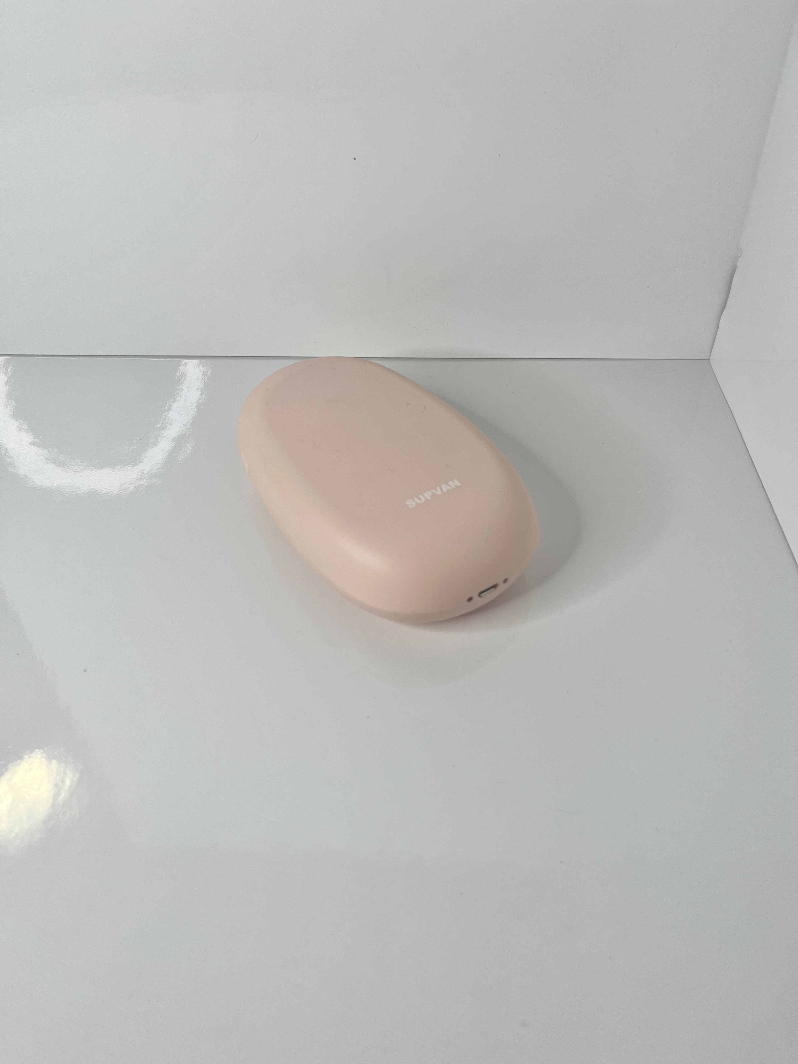 A smooth, oval-shaped portable sticker printer in pale pink rests on a glossy white background