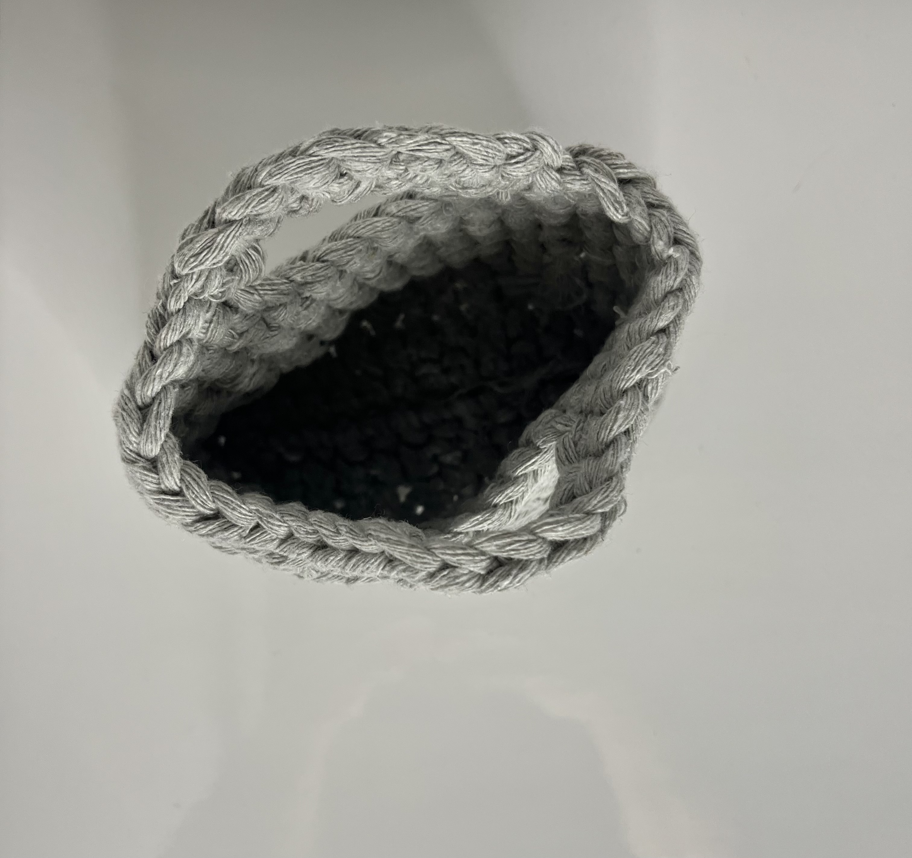 A hand-crocheted gray mini bag is photographed from above, showing the open circular weave and hollow interior.