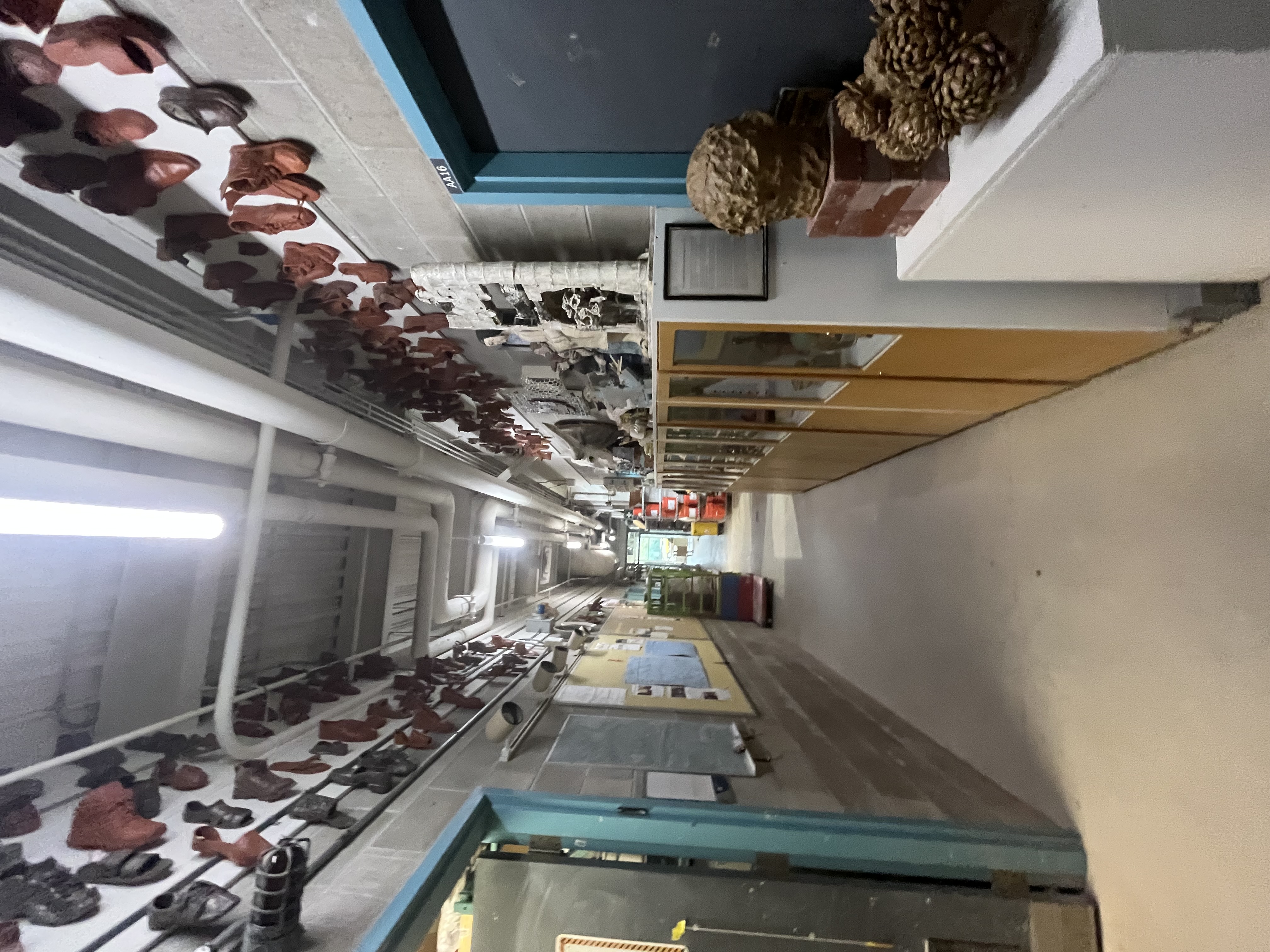 A long studio hallway displays student-made ceramic masks along the ceiling and showcases filled with sculptural works and material studies.