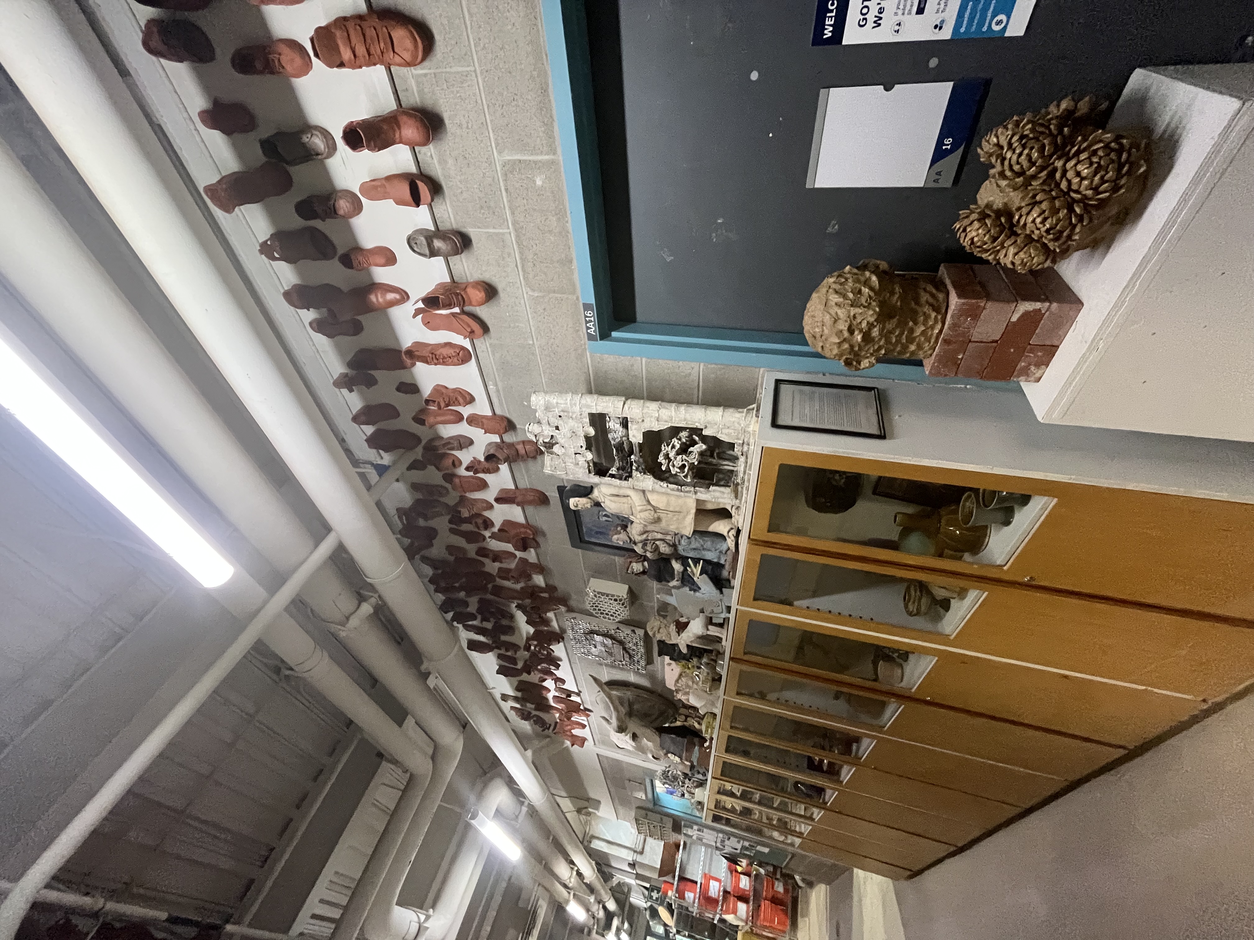 The hallway features an extensive ceramic shoe installation overhead and display cabinets showcasing a range of student-made ceramic vessels and sculptures.