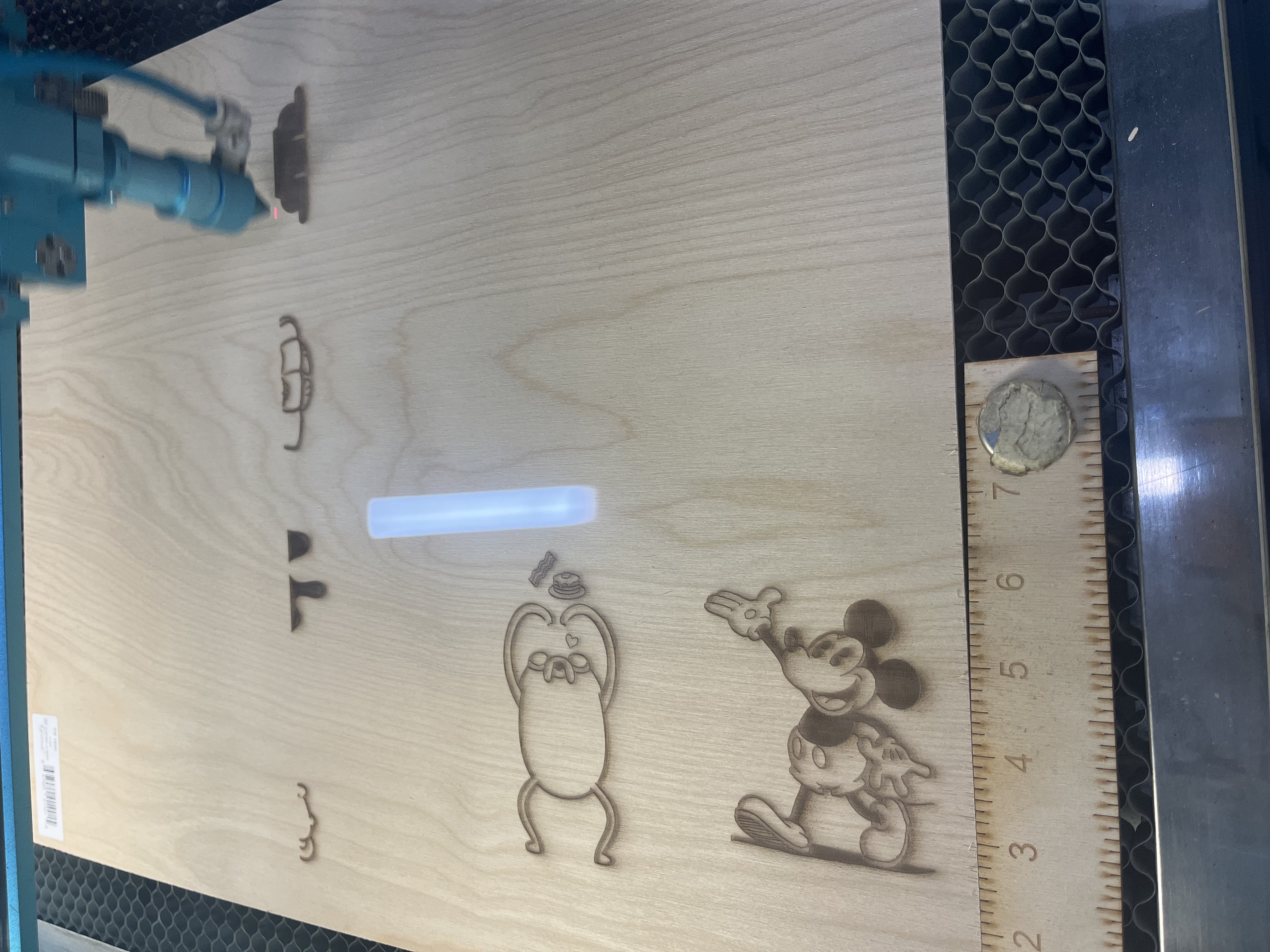 The cut sheet shows phone-stand panels outlined with fine laser-cut borders, alongside engraved character artwork centered within each piece.